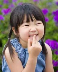A young child smiling with finger to her mouth