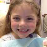 A happy young girl wearing a cat's ears barrette is smiling from the Dr. Chan's dentist chair