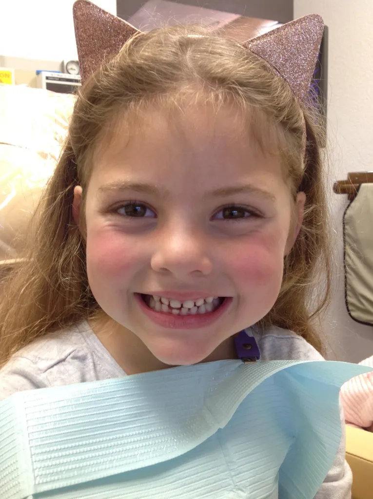 A happy young girl wearing a cat's ears barrette is smiling from the Dr. Chan's dentist chair