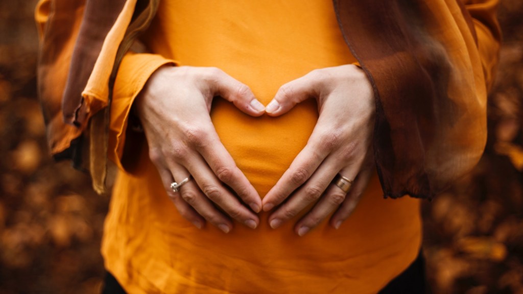 Pregnant woman making a heart shape with her hands on belly